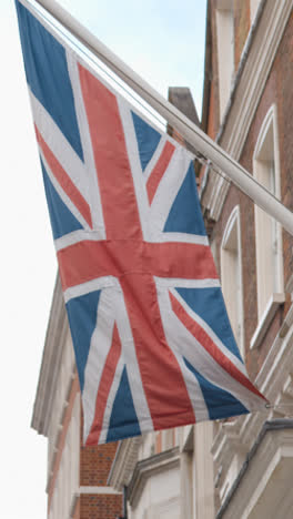 Vertical-Video-Close-Up-Of-Union-Jack-Flag-Flying-On-Building-In-Grosvenor-Street-Mayfair-London